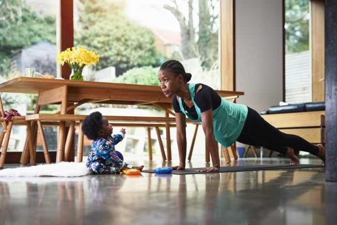 mother doing yoga in living room with baby sitting nearby