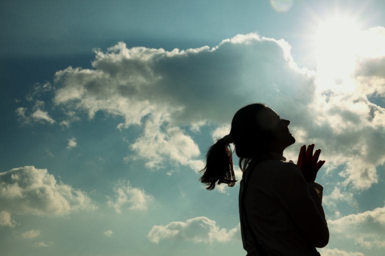 silhouette of woman looking at sun through clouds