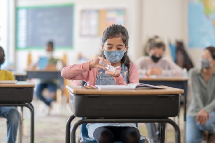 elementary classroom with girl masked and using hand sanitizer