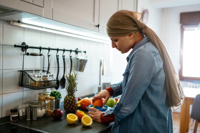 woman with cancer wearing headscarf in kitchen squeezing oranges