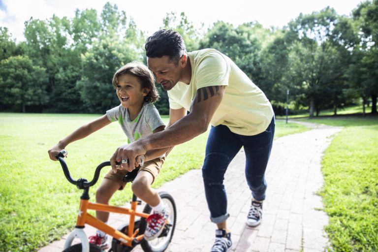 happy father teaching son to ride bike in park