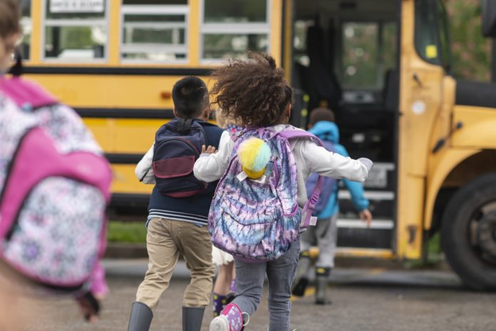 school children wearing backpacks running to school bus