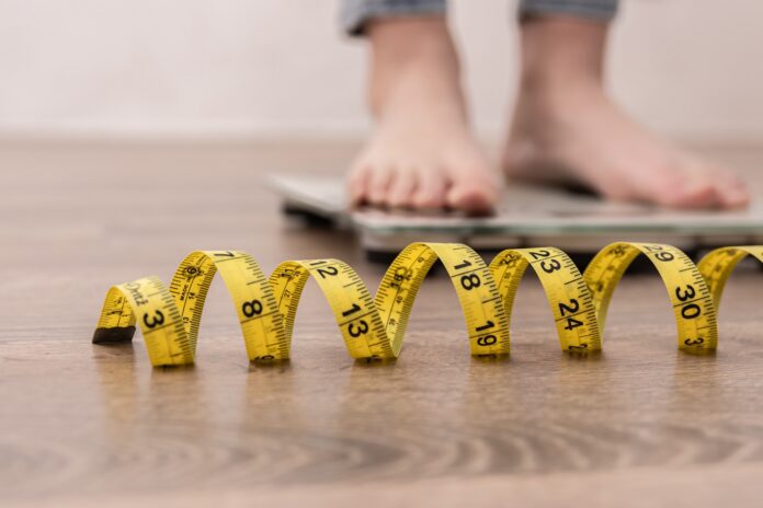 person's feet on scale with measuring tape in foreground