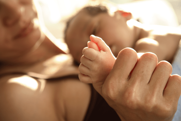 infant laying on mother and holding her thumb